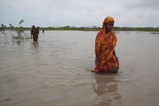 DAKKIN PATIL BARI, BANGLADESH - August 2011. In the last fortnight the Jamuna River has swollen from heavy monsoon rainfall causing severe flooding on the char islands. Women on Dakkin Patil Bariare forced to wade through the waterlogged land.