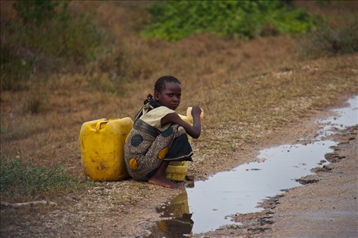 A young girl collects rainwater from the side of the road.