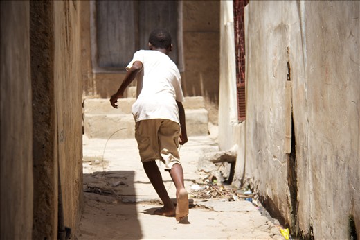 A young boy hoop rolling through the alleys of Lamu, Kenya's old town. 