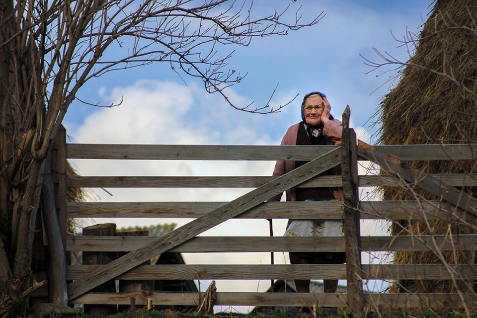 I took this photo in Durău, a town located at 780-800 m altitude in Neamţ County at the proximity of Ceahlău Massif. The location is disadvantaged because of the lack of accessibility since 2006 because the main route was closed due to landslides.
Durău counts few inhabitants that are mainly devoted to agriculture and sheep-farming. There is also a beautiful orthodox monastery founded in the XVII century, where people from all the county go to celebrate the Easter mass.
This old woman is 88 years old and still works at the farm taking care of animals. She was very kind and happy to receive some visitors. Although she didn't speak much, her eyes were very soulful.  She lives with her son, a 70-year-old sheep-keeper, and his wife. Thanks to this and other encounters during the journey in Durău, I could experience the humility of a simple life lived in harmony with nature.  