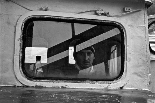 During the travel from Durău to Iaşi, the driver needed a break and so he stopped at Bicaz lake for half an hour. I decided to have a walk and see if I could meet someone in this place surrounded by high pines. I saw a carpenter and talked to him using the very few Romanian words that I learnt during my travel. It was a surprise when that middle-aged man replied to me in Italian. After a nice conversation I accepted to pay for a trip on the lake. However before going on board he explained me that, unfortunately, a big factory discharges the industrial waste into the lake. He called his friend who works as a taxi-boat driver for the local and there I met the young man that you see in the photo. After having faced the disappointing big amount of garbage, the young man invited me inside the cabin since I was freezing. Despite the difficult communication since he spoke only Romanian, he explained me that the boat is his only house. He opened the door behind him and showed me his tiny room with a little bed and few objects. He then told me that he doesn't want to leave the lake of Bicaz and that he is happy with his life.