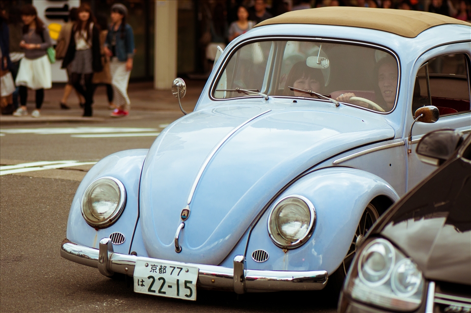 A couple drives through downtown Kyoto in their vintage, 60's era Volkswagen Beetle.