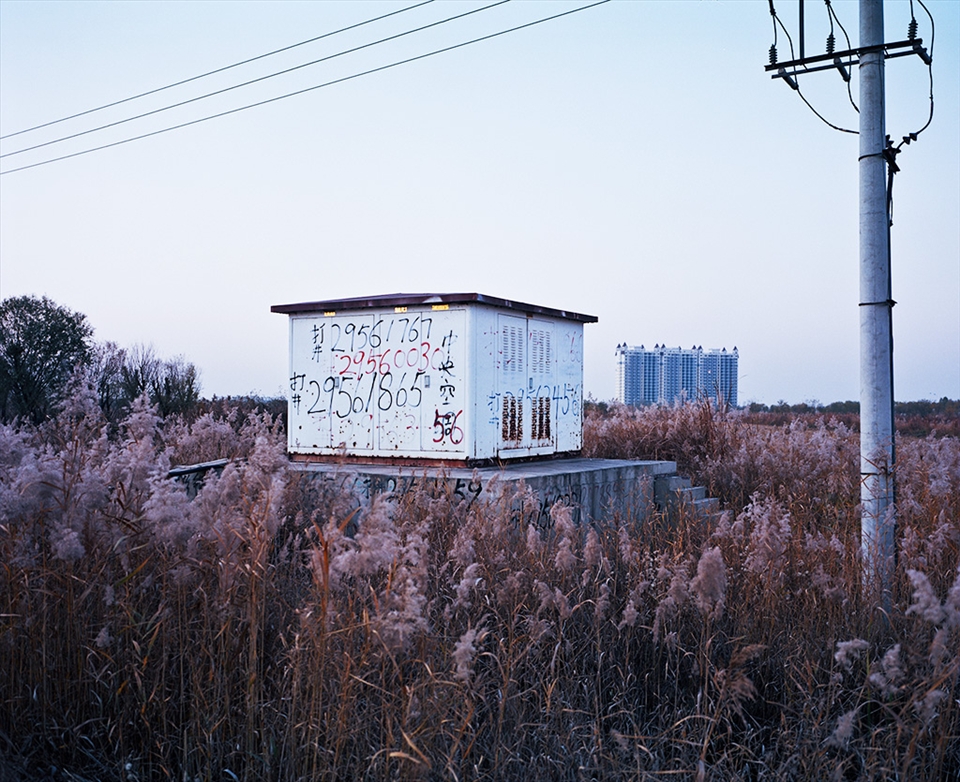 Graffiti advertises the services of local tradesman looking for work in Jing Jin, plastered on a transfer box that sits in the shadow of an abandoned high rise building in the middle of nowhere. The simple messages consist of a job description (eg. 'roof tiler') and a contact phone number. The desolate fields surrounding Jing Jin mirror the emptied ghost town of the city itself.