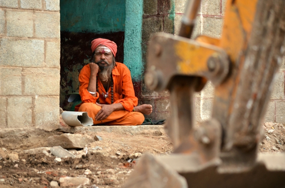 A Sadhu sits at his doorstep observing the grave destruction surrounding him as the homes of his neighbors are leveled out. This action was orchestrated to enable visitors to experience the ancient structures as they existed centuries ago.