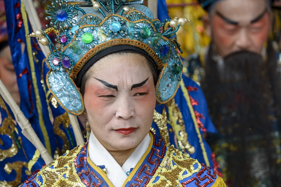 Beneath the omnipotent gaze of a statue devoted to the clan god, costumed performers wearing imposing Chinese opera face paint and stunning sequined outfits begin a choreographed procession in the temple’s entryway.  As the band strikes up a cacophonous clanging of drums, flutes and cymbals, the actors begin wildly circling the offering table. With their costumes fluttering from harnesses in a blaze of primary colour, the troupe’s otherworldly performance is reminiscent of a whirling flock of mystical birds. 