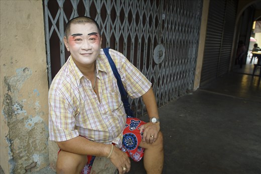 Birthday celebrations continue throughout the day with a feverish schedule of music, concerts and offerings. A Yap clan performer assumes a more casual pose away from the heat and commotion at the temple. Just moments earlier, he had formed a picture of ancient wisdom in fake waist-length beard and elaborate headdress. The actors are not professionals, but merely familial revellers, friends-of-friends and neighbours enjoying their moment in the spotlight.