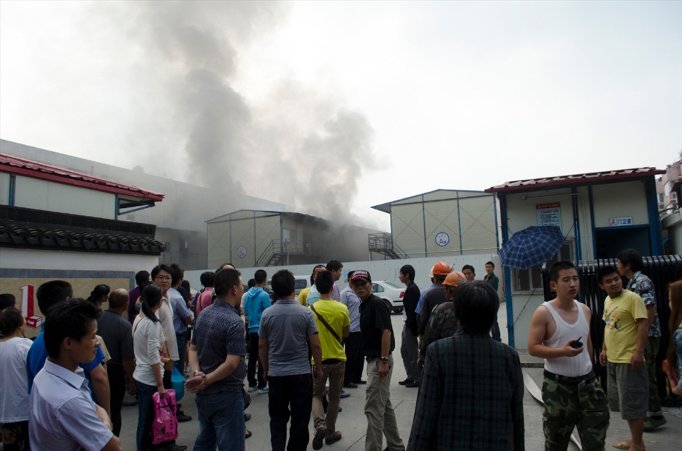 A crowed of local Chinese gather around as large pillars of smoke start emanating from a nearby building.