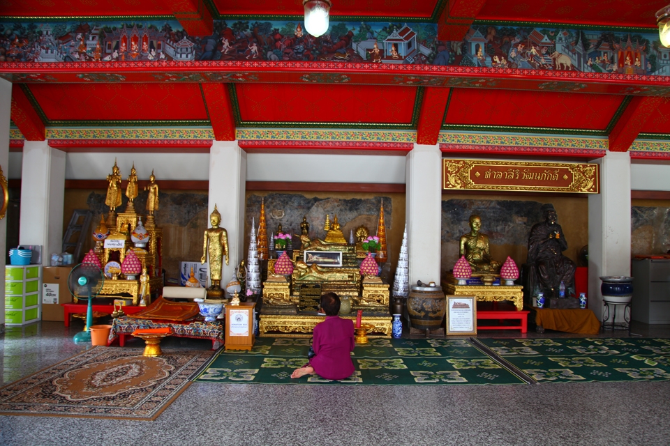 A woman is praying in a temple which is full of sculptures and wall-paintings.