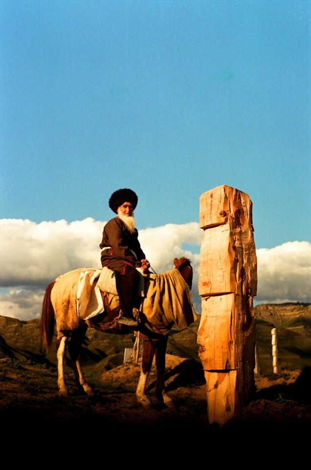 As high as the nature, facing death. An old man stands in a cemetery looking at his relative’s grave.