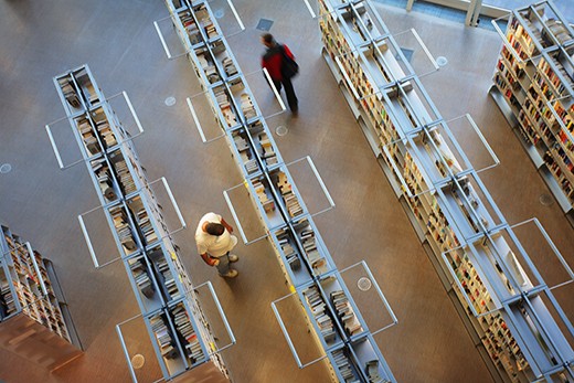 A person is searching books on the book shelve, and another person is walking through. (Seattle Public Library)