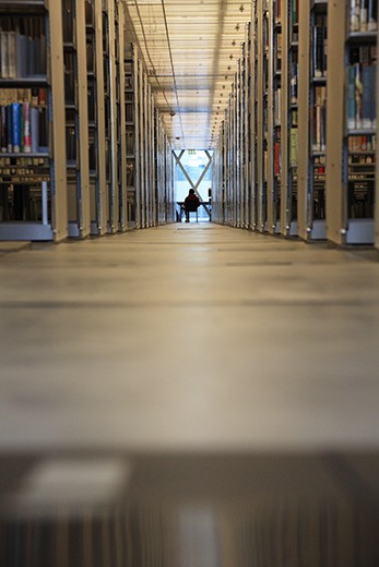 A man is reading at the end of the aisle, surrounded by tons of books. (Seattle Public Library)