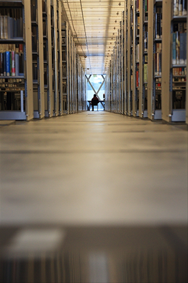 A man is reading at the end of the aisle, surrounded by tons of books. (Seattle Public Library)