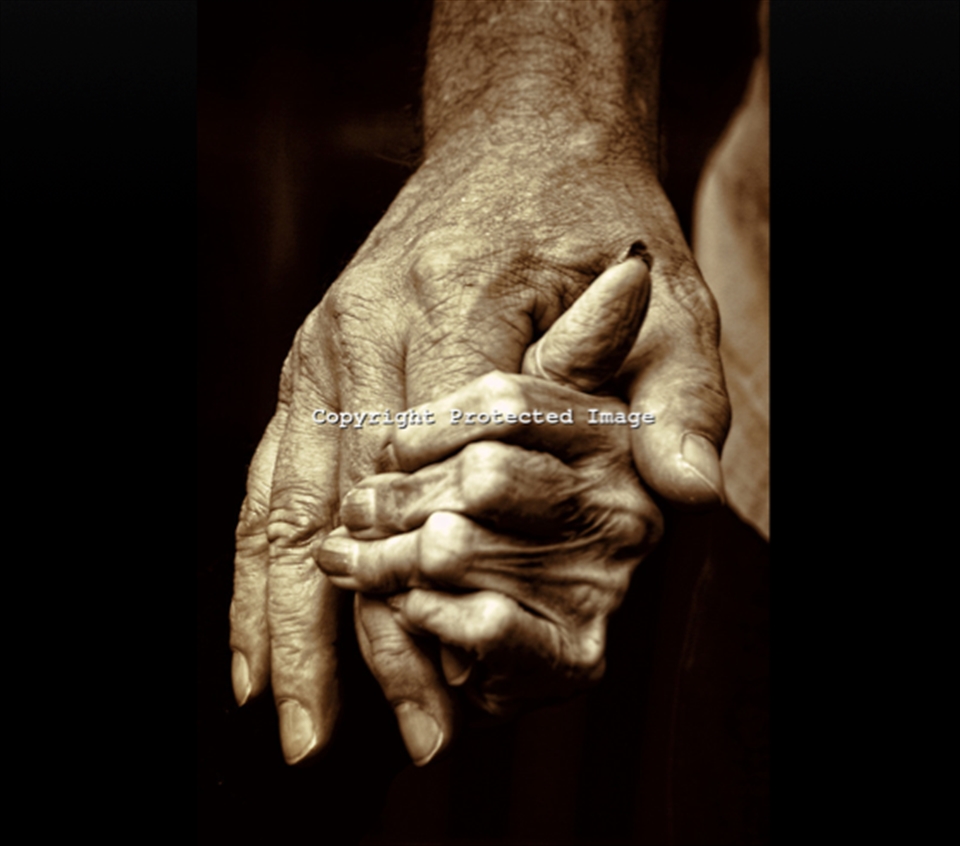 Not ever wanting to let go, a son grasps the hand of his aging mother at a nursi