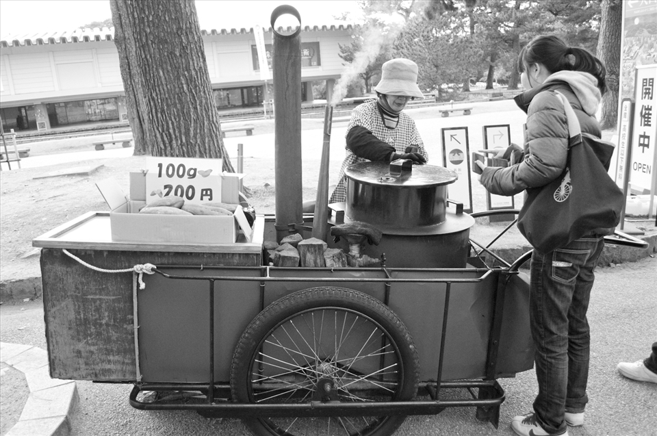 Old granny selling hot baked sweet potato in cold winter days.