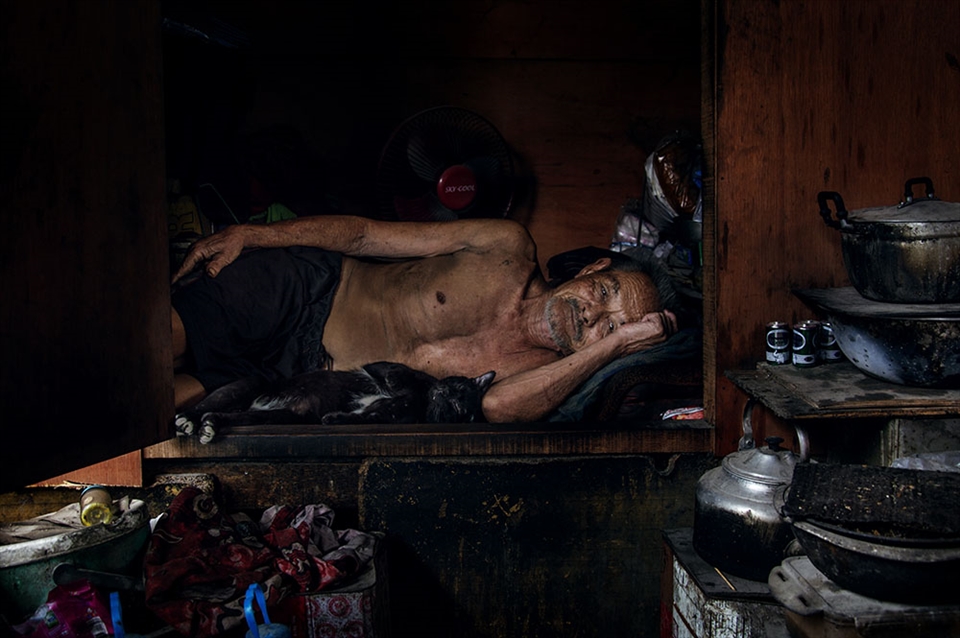 Man rests in his wooden house with pet cat to escape the heat of the day.