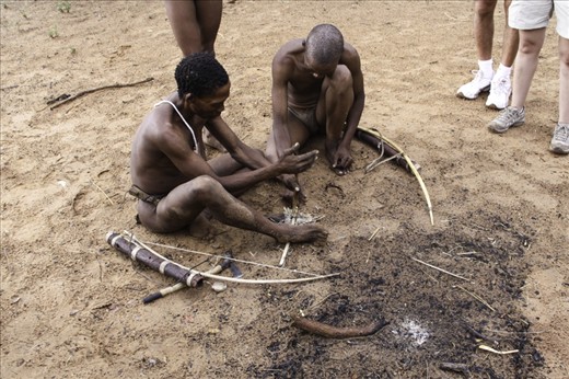 A San shows the traditional way of starting a fire, rubbing 2 sticks together. This is harder than it looks, you must generate enough friction for the tinder to start smouldering. There had been a large storm before this was taken but he had no problems with the wet conditions.