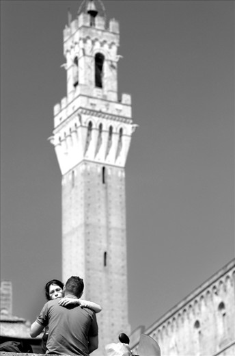 A young couple embrace in Siena, Italy under the backdrop of the Torre del Mangia. The Torre is the last standing tower in Siena. 