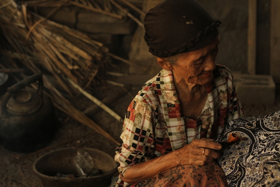 An old woman diligently paints batik patterns on cloth in a half built house in the village of Bantul, DIY. She earns five $2-5 for each batik cloth, which is then sold to the middleman who sells it to public markets and foreigners for $30-50.