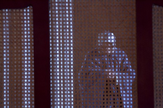 A woman praying in a small room with a screen at the back of the mosque.