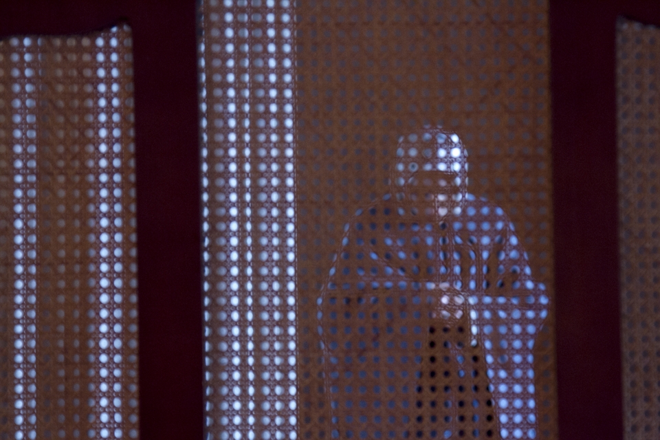 A woman praying in a small room with a screen at the back of the mosque.