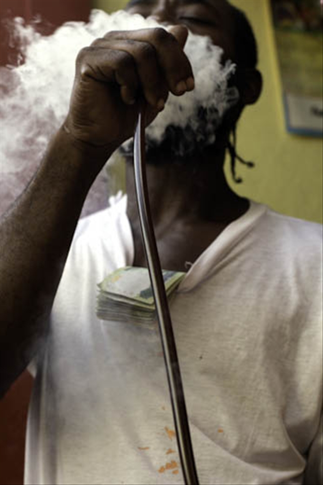 Another descendant of the Swallow Field garrison community takes a much needed smoke break from the running of his Ital Food Restaurant. He puffs on a chillum pipe with a wad of local $1000 notes purposely tucked into the neck of his t-shirt.