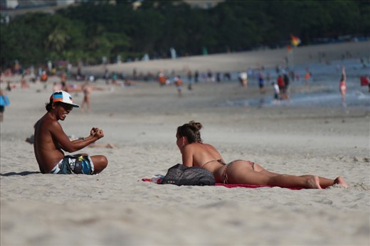 Local young man speaks with a tourist while she rests on the beach, in Bali, Indonesia.