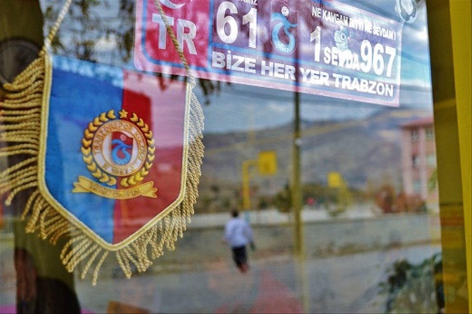 Title: “For us, everywhere is Trabzon”
The passion for sport is also a mark of Anatolian people. Here, the symbol of Trabzon football team and a sign with the words in turkish “Bize her yer Trabzon”, that means “For us, everywhere is Trabzon”, referring to a city in the Black Sea. In the reflected image there is a late student running to reach the school after the break. Tortum Village, Eastern Anatolia of Turkey, November of 2012.