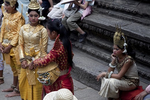 A girl dressed in traditional Khmer costume gets off her feet in between costumers. A steady stream of tourists pays one dollar each to photograph her troupe. With over 1 million visitors to the site each year and rising, increased opportunity for employment comes with the price of site degradation.