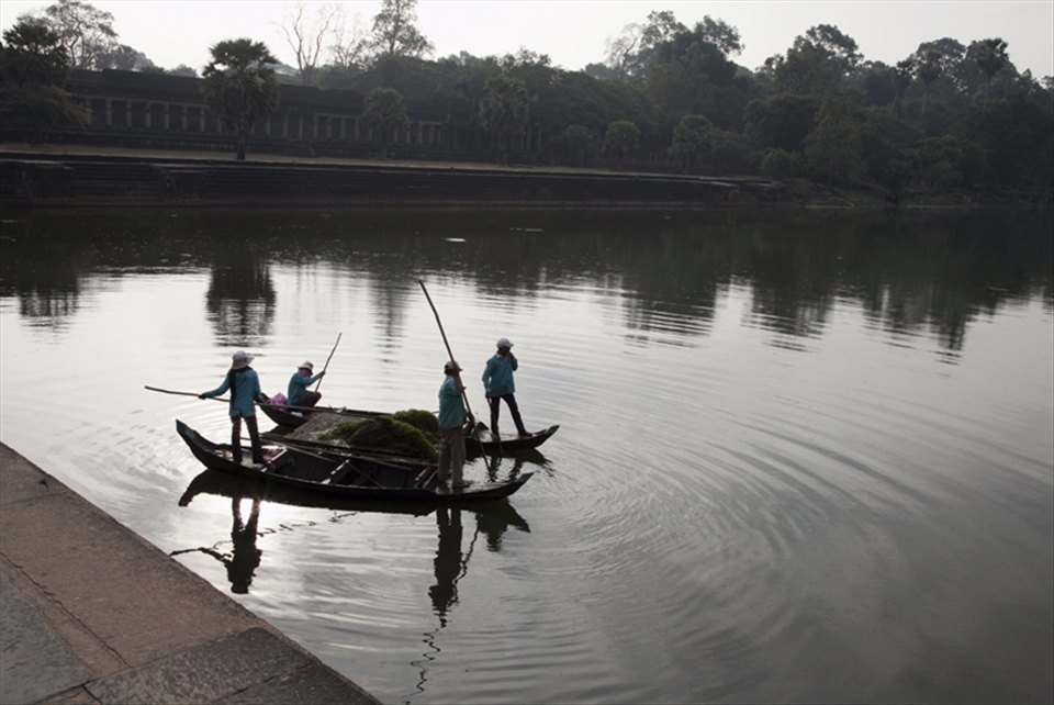 Groundskeepers make their way across the waters that surround the temple. This ancient moat structure, excavated by hundreds of thousands of workers, is so big that it’s visible from space.