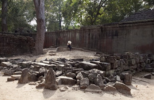 Surrounded by 12th century rubble, a guide takes advantage of a quiet moment to text. In 1992, Angkor Wat was placed on the List of World Heritage in Danger due to illegal excavations, but was removed in 2004 after successful preservation initiatives.