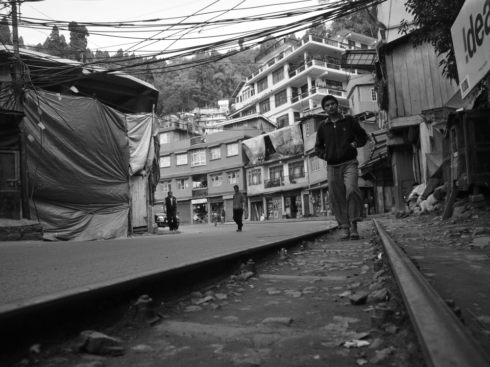 Darjeeling also known as the 'Queen of the Hills' is a town situated at an altitude of 6710 ft. in the Indian state of West Bengal. Under immense pressure from the Tea and Tourism industry, dense greenery of the hills is replaced by tea gardens and concrete structures. Seen above in the image is the tracks of the Darjeeling Himalayan Railway- a World Heritage Site which leads up to the Chowrasta Square popularly known as The Mall.