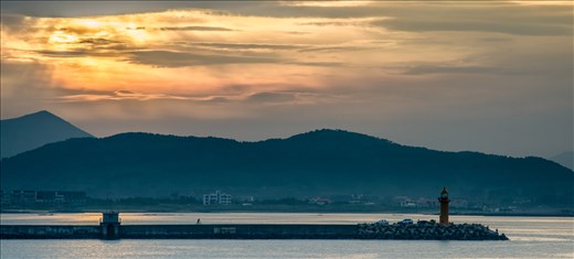 A Man rides a bicycle out to the lighthouse where local fisherman gather at dusk
