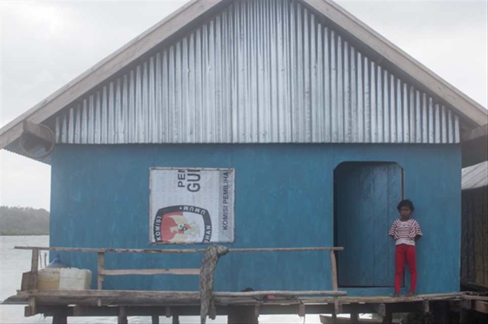 A young Bajo girl stands outside her home watching foreign visitors walk by.