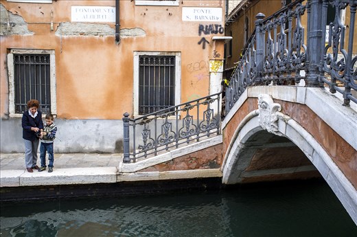 A grandmother helps her grandson fish in the canals of Venice.