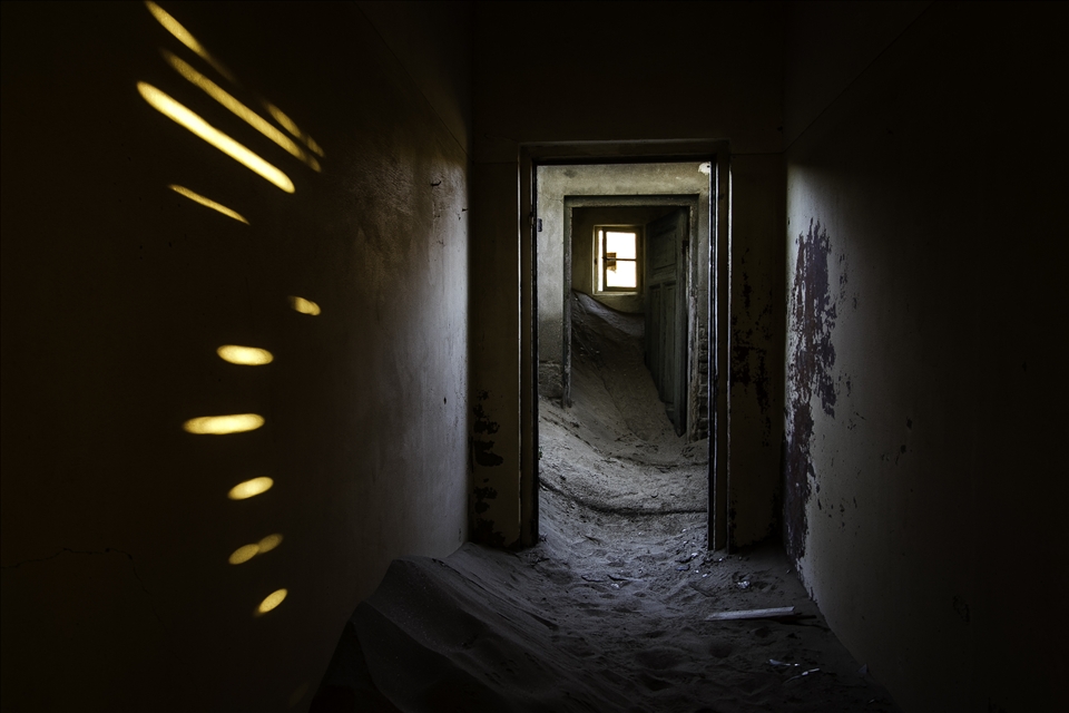 Bright desert light shining through wall cracks and missing windows gives the houses an eerie, surreal, and dramatic atmosphere  