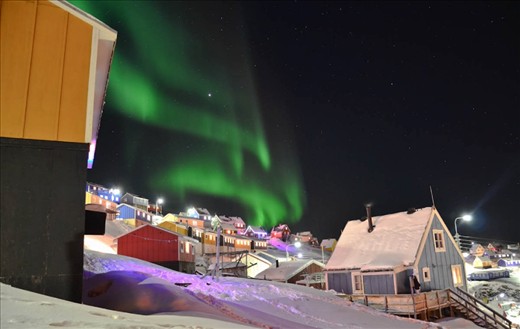 This one was taken in Upernavik, Greenland. 
I was in a hurry to go to an airport for a flight when I just suddenly caught a glimpse of a good spot to capture that moment.  The northern lights were moving in a beautiful wavy way and in addition the town was quiet, no people in streets. There was lots of Christmas lights mixed  in the town, because it was just after Christmas when I arrived there.  With everything I mentioned before, this photo is beautiful.