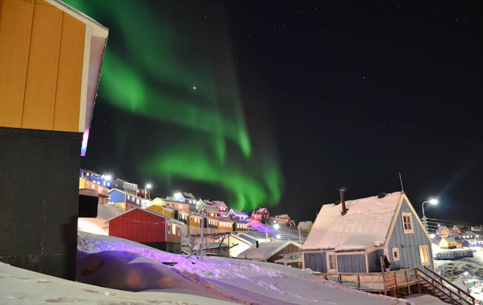 This one was taken in Upernavik, Greenland. 
I was in a hurry to go to an airport for a flight when I just suddenly caught a glimpse of a good spot to capture that moment.  The northern lights were moving in a beautiful wavy way and in addition the town was quiet, no people in streets. There was lots of Christmas lights mixed  in the town, because it was just after Christmas when I arrived there.  With everything I mentioned before, this photo is beautiful.