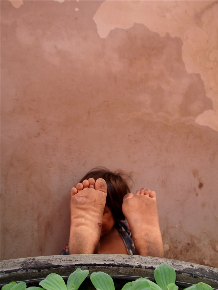 'little feet' - taken in the rural town of Kampot, South Cambodia. This shot was from a series of photographs taken. It is of a little girl who at the time was playing crazy with her sister. So happy but worn out, she takes refuge in sitting down behind this large pot to put her feet up. priceless.