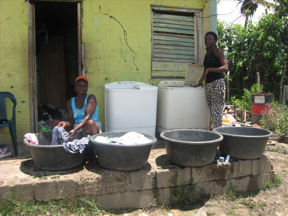 Two women washing clothes by hand next to previously donated  washing machines. The scene seemed odd, and I wondered why they were not using the appliances. I later learned they simply could not, as the machines were not adapted to their living conditions. 