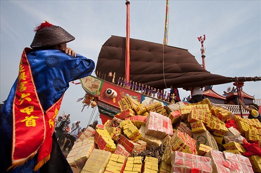 
In a circle of three years a number of temples in Taiwan practise a old ritual where big beautiful boats are build to be burned once completed.
The origin of this tradition is dating back to the 18th century when a crew less boat arrived on shore. People who discovered this boat held it for a ghost ship and filled it up with all necessities on sea and send it back to where it came from. It became a tradition to build a boat and pack it with lots of goods such as food, drink, valuables and even games for entertainment and burn it after all bad spirits of the neighbouring towns been brought on board as well. At some point in history they start to burn the ship rather than send it out to the sea because of the bad spirits such as sickness they put on board, it has been considered that the ship will get on land at some other point and will bring evil to the people there.
On the first image a village leader takes a careful look that no mistakes are made during the loading and preparation of the ship. There are many rules and orders to be respected to assure all evil spirits will be gone after the boat is burned. 