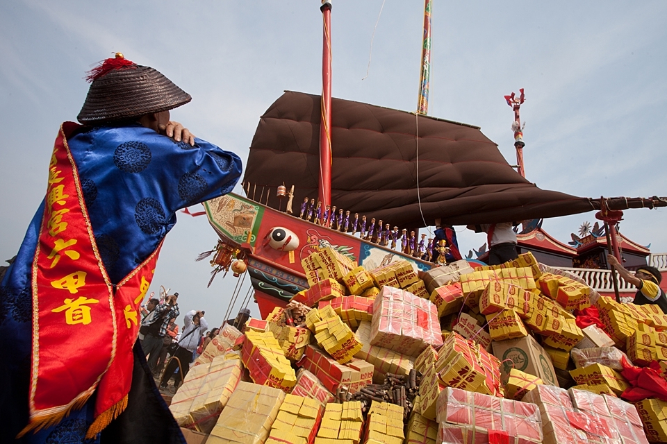 
In a circle of three years a number of temples in Taiwan practise a old ritual where big beautiful boats are build to be burned once completed.
The origin of this tradition is dating back to the 18th century when a crew less boat arrived on shore. People who discovered this boat held it for a ghost ship and filled it up with all necessities on sea and send it back to where it came from. It became a tradition to build a boat and pack it with lots of goods such as food, drink, valuables and even games for entertainment and burn it after all bad spirits of the neighbouring towns been brought on board as well. At some point in history they start to burn the ship rather than send it out to the sea because of the bad spirits such as sickness they put on board, it has been considered that the ship will get on land at some other point and will bring evil to the people there.
On the first image a village leader takes a careful look that no mistakes are made during the loading and preparation of the ship. There are many rules and orders to be respected to assure all evil spirits will be gone after the boat is burned. 