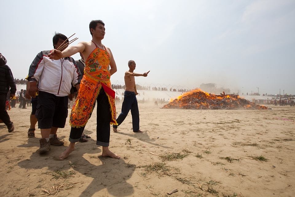 The heat of this immense fire is massive and so the circles the crowd walks around the fire become larger and larger. After the show down of the falling masts the priests, the musicians, the carriers of relics and the village chiefs with there followers as well as the obsessed mediumship's as seen on this image, make three more circles around the fire and than disappear in all directions. Mediumship (known as mediums) are man who mediate communication between spirits of the dead and other human beings.