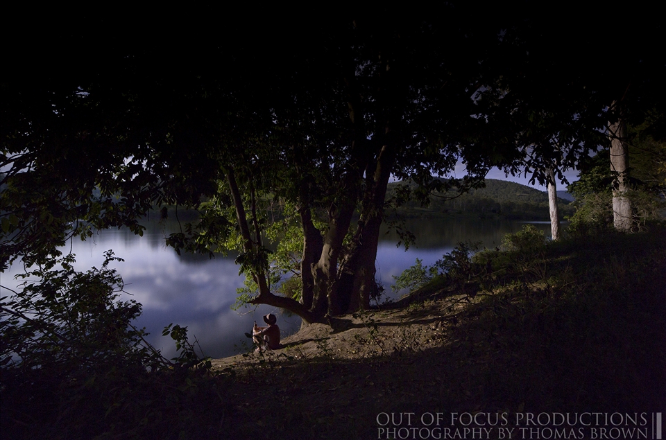 A stranger sitting on a river bank having a drink during a full moon.