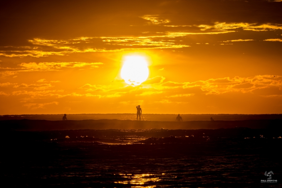 The day is just starting and surfers alike are already in the water patiently waiting for a chance at that perfect ride.  Heading out into the breakers is a stand up paddle boarder trying to navigate his way as the surprisingly harsh sun rises from beneath the clouds.