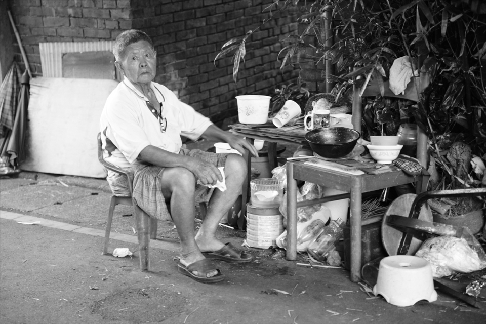 Every dawn, he sits on the plastic chair with the wooden chair as his dinner table and consumes his dinner out there in the alley.  The man had just finished his dinner then.