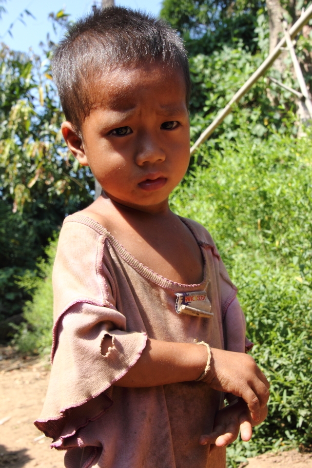 Taken at Mae Saut Noi  village in  Mae Sariang - Mae Sot area in Thailand, the people are of the Karen tribe they are one of the many ethnic groups from Burma and have moved from their villages from Burma escaping the civil war conflict against them by the Burmese Military or extreme poverty their life's are much more free in Thailand than in Burma where it's very dangerous over their. 

This is one of the very few villages that are still very traditional way of living very simple life, they have no electricity or technology but they are happy living like this in their cozy bamboo huts. The kids play outside all day everyone cheeps in like washing clothes, cooking ect. The environment/hygiene isn't that clean as they are quite poor. It was a great and very nice atmosphere something that I have never experience before.

The young child in the photo was kind of shy but soon giggled at the sound of my slr camera clicking. The clothing of the child was pretty dirty and old and looked a bit to big on the boy as the living conditions in rural villages hygiene is not the best, but kids are kids they like to play and get dirty.

I captured mainly children in this rural village they were very excited seeing a foreigner and were most interested in my big slr camera as I was clicking away. 