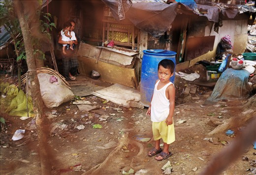 A child stands in front of a house made of years worth of scavenged materials 
