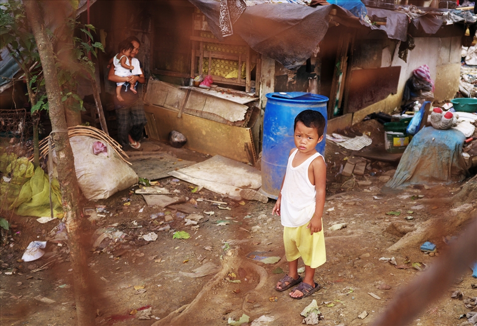 A child stands in front of a house made of years worth of scavenged materials 