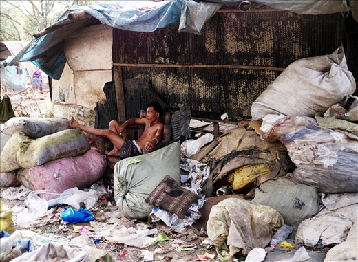 A man listens to music as he lounges on a shabby sofa amidst mountains of trash