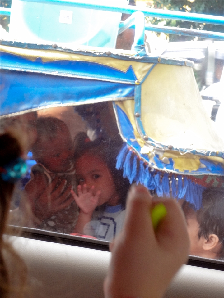 One of the several children all crammed into a tricycle with their parents shares a moment with my 3 year old sister before motoring off into the chaotic haze of local traffic.